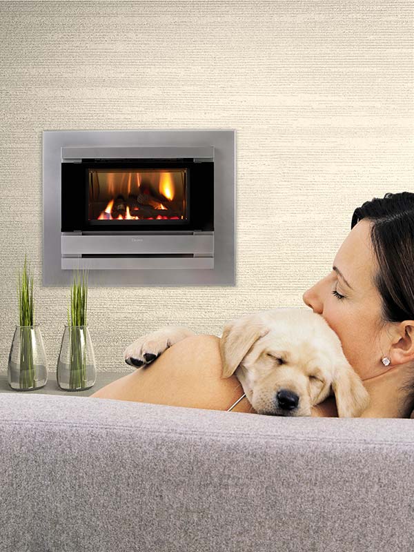Cannon Fitzroy Powerflue Gas Log Fireplace 4-Sided Platinum Surround with a woman and puppy on lounge